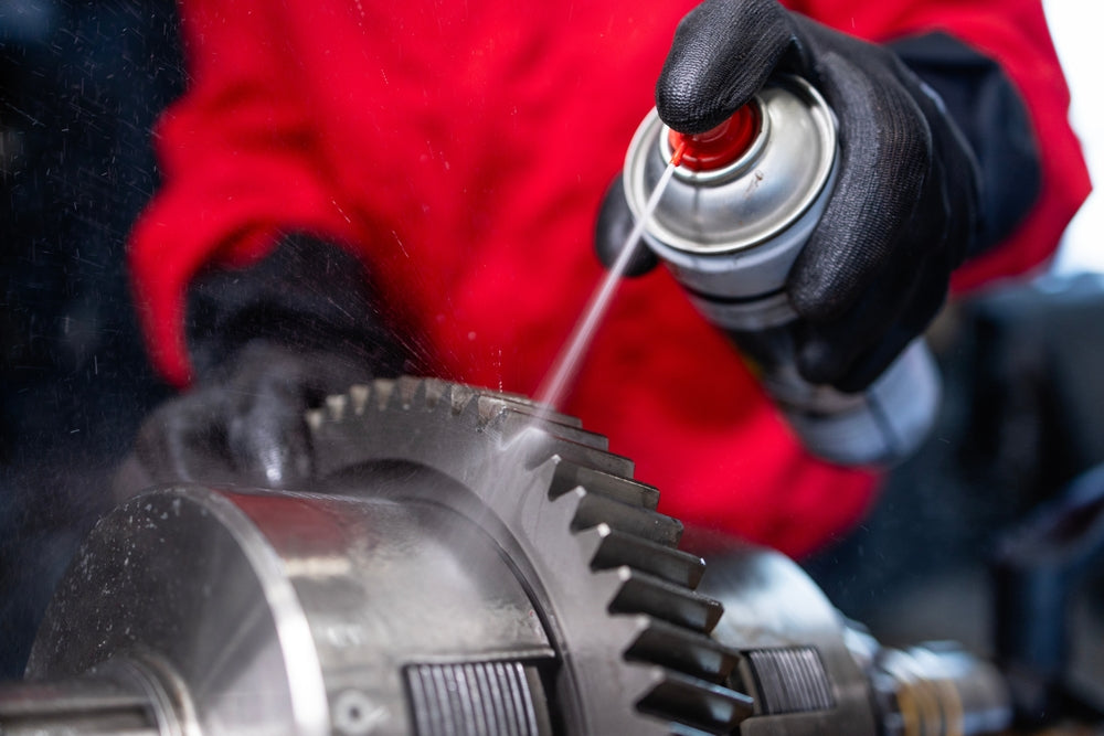 Serviceman spraying and lubricating transmission gears in workshop