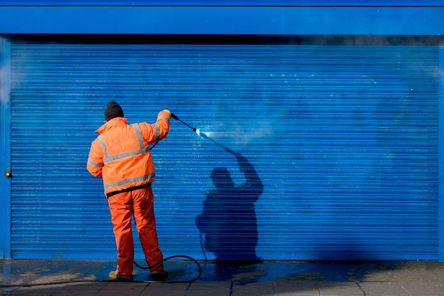 Person in orange safety suit cleaning graffiti with a pressure washer.