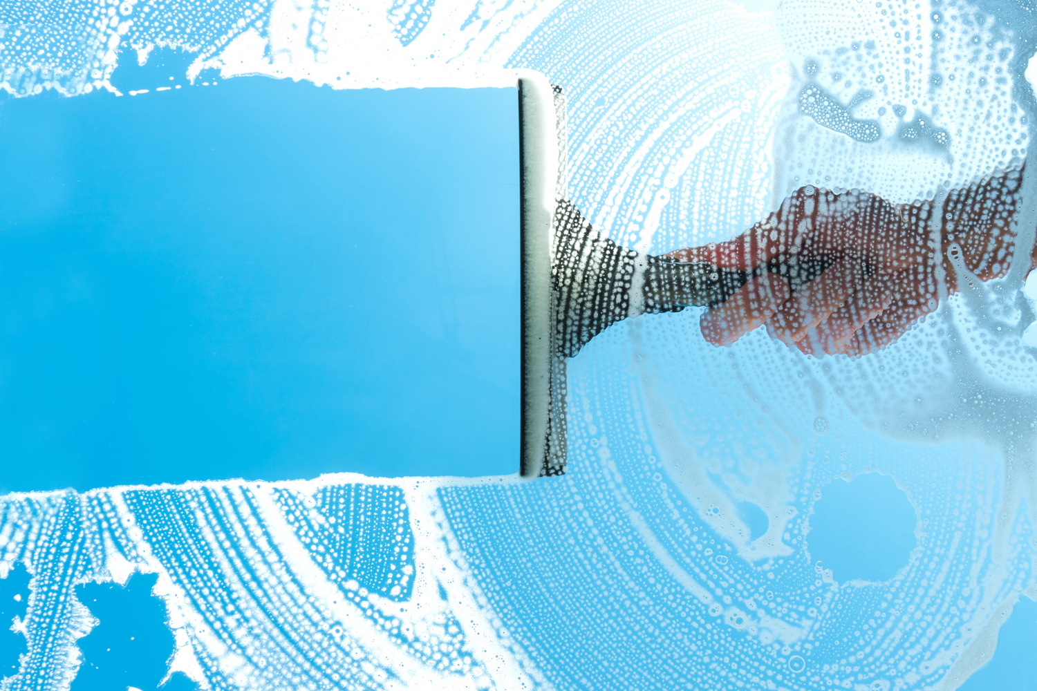 Hand cleaning a glass surface with a squeegee, surrounded by cleaning residue.