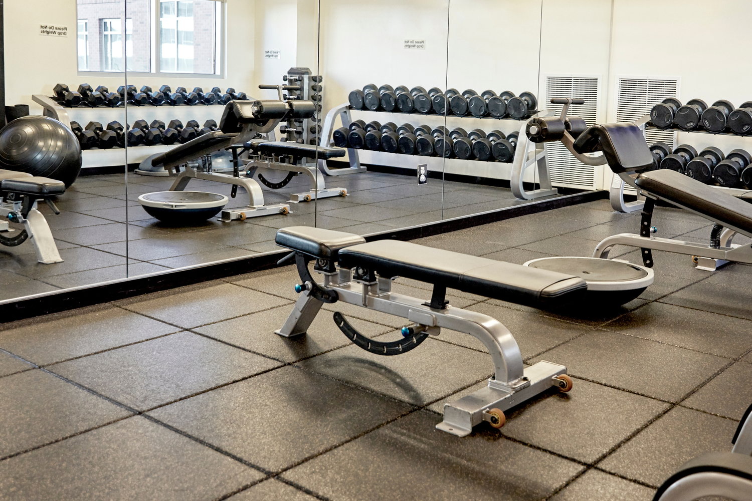 Gym interior with weight machines and free weights on a tiled floor.