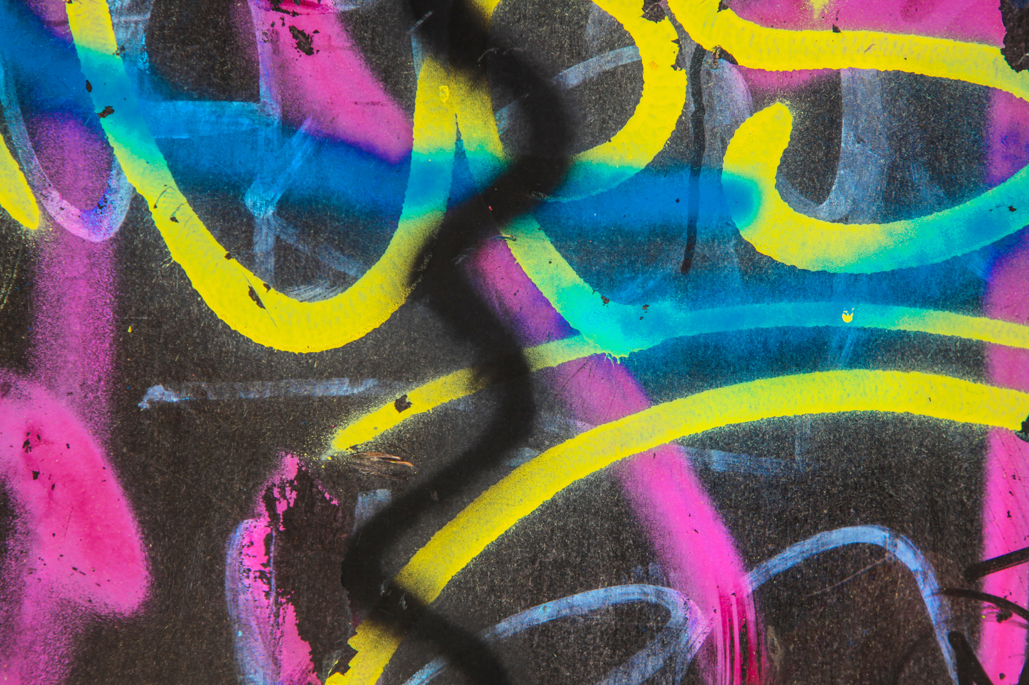 Close-up of colorful graffiti on a wall with vibrant pink, yellow, blue, and black colors.
