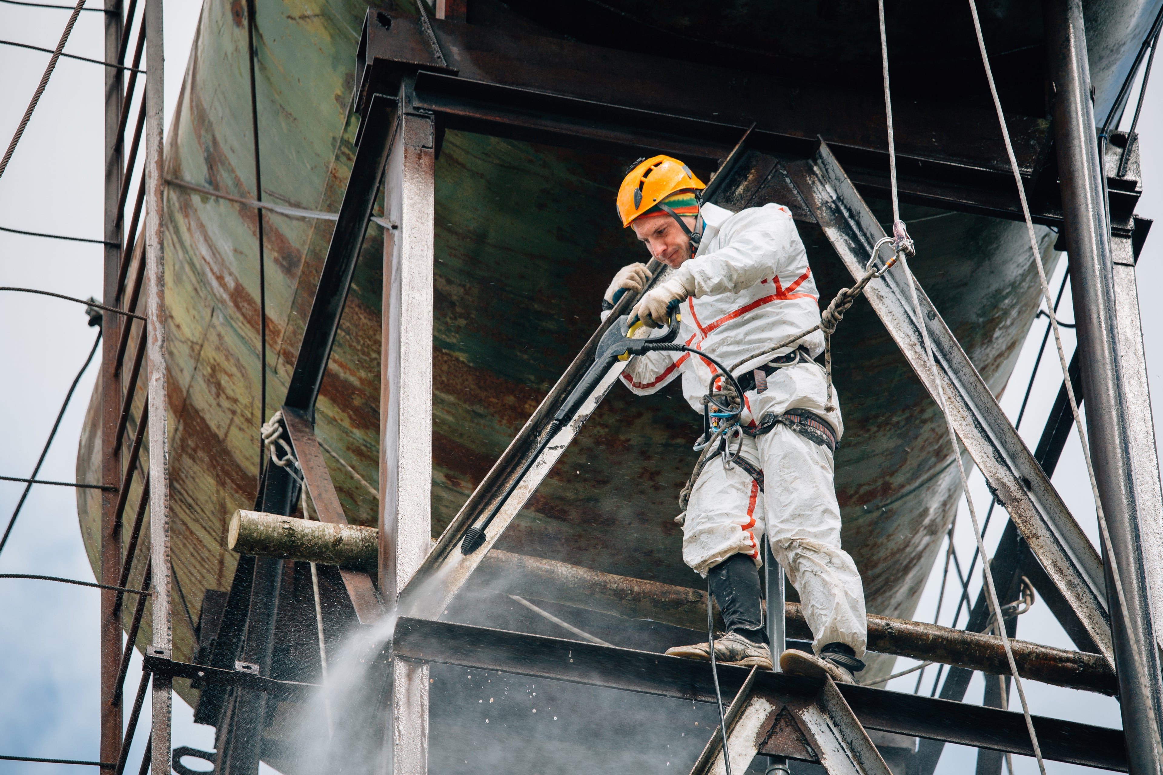 Industrial climber washing big barrel with water pressure