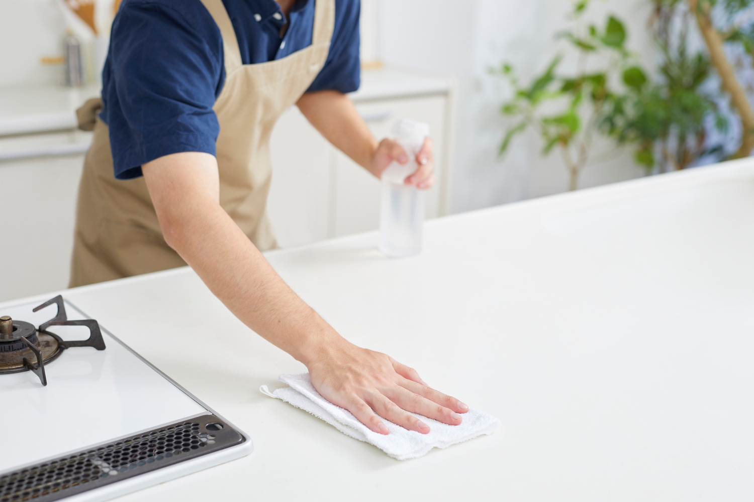 Person cleaning a kitchen counter with a cloth and spray bottle.