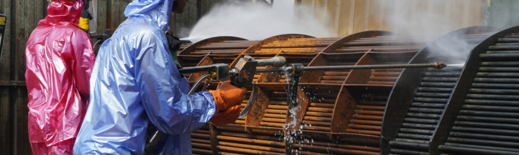 Workers use a high-pressure water jet to splash away dirt from pipe bundles in industrial areas, chemicals or oil and gas plants.