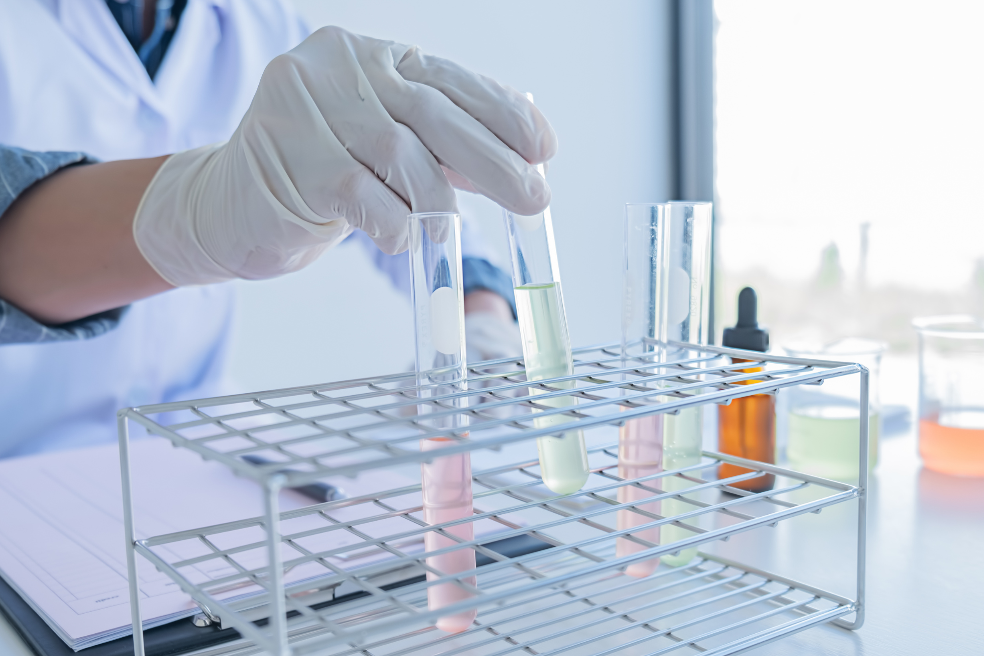 Person in a lab setting holding a test tube with a rack of other test tubes in the background.