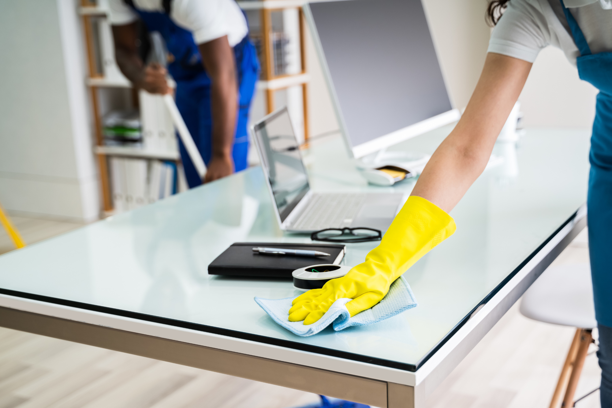 Person cleaning a glass desk with a yellow glove in an office setting