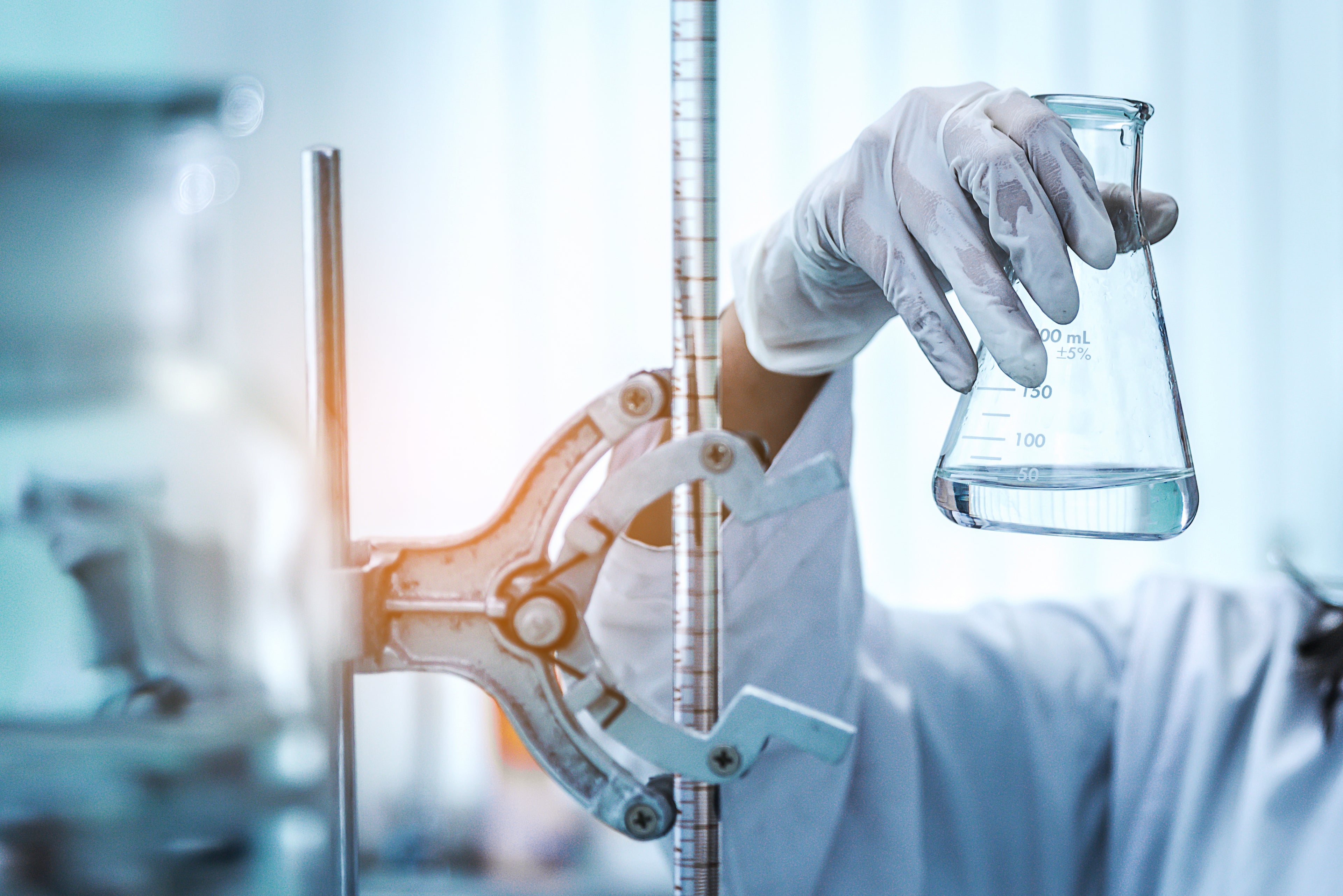 Person in a lab coat holding a beaker with scientific equipment in the background